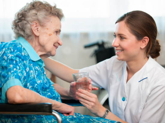 Pflegerin reicht Seniorin ein Glas Wasser